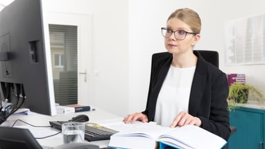 Frau arbeitet am Schreibtisch mit Computer und Buch.