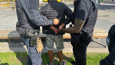 Person wird von zwei Polizisten in Handschellen gelegt.