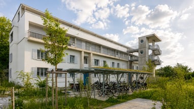 Weies Wohngebäude mit Fahrradabstellplatz und B�umen.