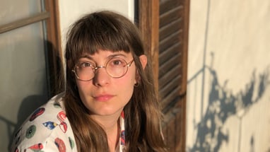 Person mit Brille schaut nachdenklich in die Kamera, Sonneneinstrahlung im Hintergrund.