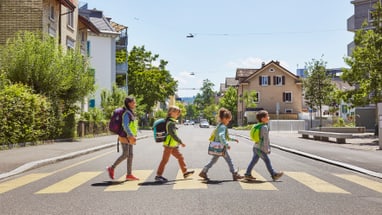 Kinder überqueren Zebrastreifen in Wohnviertel bei Sonne.