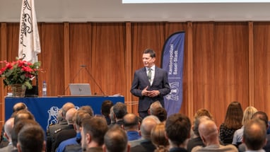 Mann hält Vortrag vor Publikum in einem Saal.