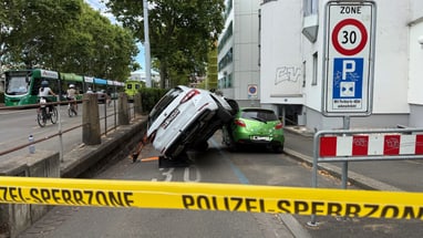 Ein Auto ist auf seiner Seite gekippt und ein anderes Auto steht daneben, mit einem Polizeiband im Vordergrund.
