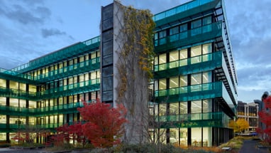 Modernes Gebäude bei Dämmerung mit Glasfassaden und Herbstbäumen.