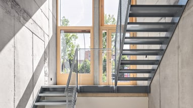 Moderne Metalltreppe in Betonraum mit grossen Fenstern.