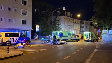 Nachtaufnahme einer Unfallstelle mit Polizei und Krankenwagen auf der Strasse.
