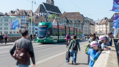Strassenbahn auf Brücke in Basel mit Fussgängern und Radfahrern.