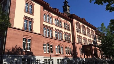 Historisches Gebäude mit Turm und mehreren Fenstern bei sonnigem Wetter.",