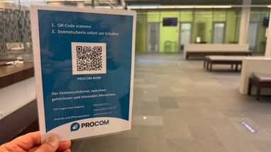 Hand hält einen Flyer in einem modernen Empfangsbereich.