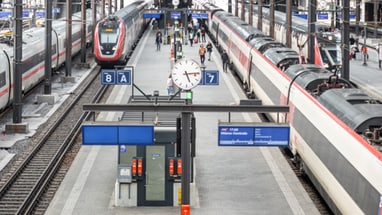 Bahnhof Basel mit Zügen und Uhr auf dem Bahnsteig.