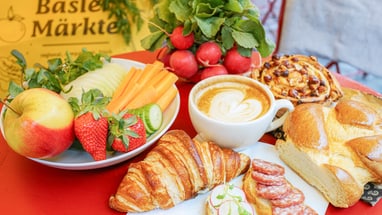 Frühstückstisch mit Croissant, Kaffee, Obst, Gebäck und Radieschen.