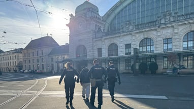 Polizisten begleiten Person vor grossem Bahnhofsgebäude bei Sonnenuntergang.