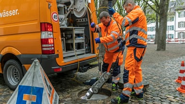 3 Männer stehen vor einem Auto und reinigen einen Abwasserkanal