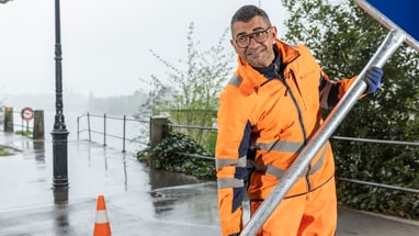 Arbeiter in orangefarbener Sicherheitskleidung hält ein Strassenschild.