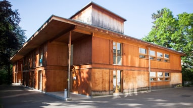 Holzgebäude mit Fenstern, umgeben von Bäumen.