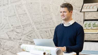 Mann mit Laptop und Landkarten auf dem Tisch.