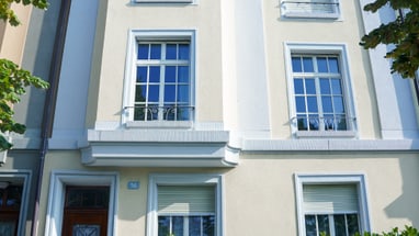 Fassade eines mehrstöckigen Wohnhauses mit Bäumen im Vordergrund.