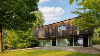 Modernes Haus mit Holzwand und grossen Fenstern umgeben von Bäumen.