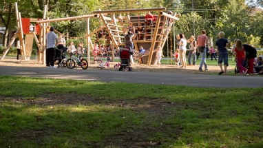 Kinder und Erwachsene im Park bei einem Spielplatz mit Holzkonstruktion.