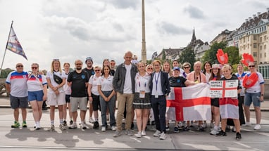 Gruppe von Menschen posiert mit Flagge auf einer Strasse in einer Stadt.