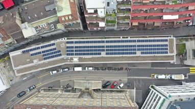 Draufsicht auf Gebäude mit Solarpaneelen und Strasse in der Stadt.",