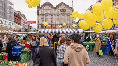 Menschen auf einem belebten Marktplatz mit gelben Ballons.