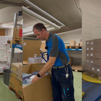 Mann in blauer Arbeitskleidung in Lagerhalle mit Kartons.