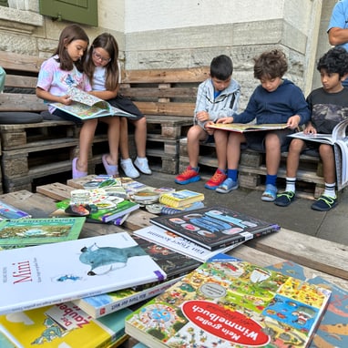 Kinder lesen Bücher auf einer Holzbank draussen im Lesegarten.