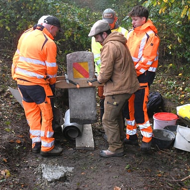 Arbeiter in orangefarbener Kleidung richten einen Grenzstein aus.