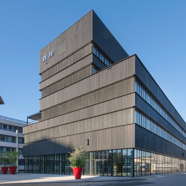 Modernes mehrstöckiges Gebäude aus Glas und Metall unter klarem Himmel.