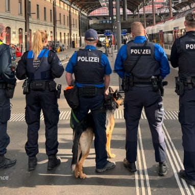 Fünf Polizisten mit Hund auf Bahnhofsplattform.",