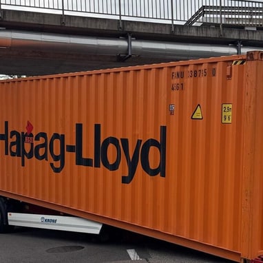 Grosser orangefarbener Container auf einem Anhänger unter einer Brücke festgefahren.