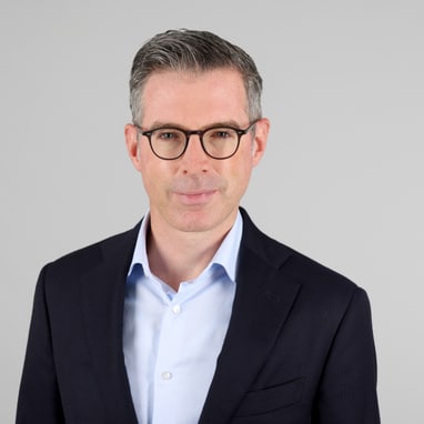 Der neue Leiter der Steuerverwaltung Basel-Stadt Thomas Beda Fischerim Anzug mit Brille vor grauem Hintergrund.