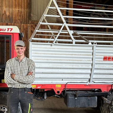 Ein Mann steht vor einem landwirtschaftlichen Fahrzeug in einem Holzgebäude.