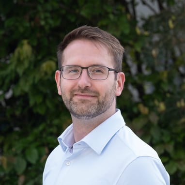 Person mit Brille und Hemd vor Pflanzenhintergrund.