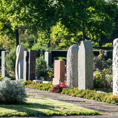 Reihe von Grabsteinen auf einem Friedhof bei Tageslicht.