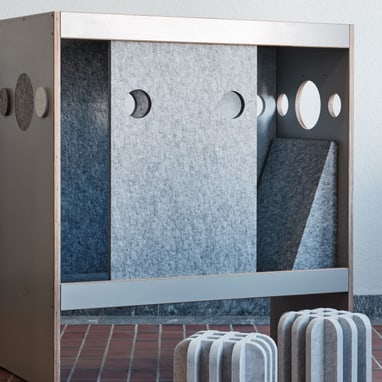 Designer-Raumteiler mit Ausschnitten und Würfelhockern auf Fliesenboden.