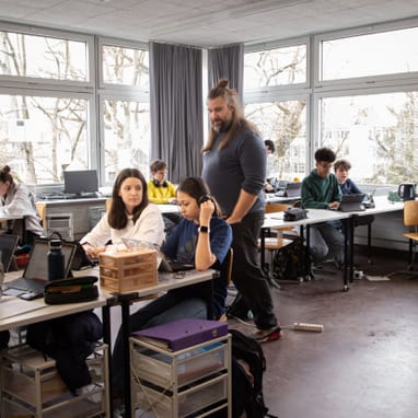 Klassenzimmer mit Schülern und Lehrer Samuel Stirnimann bei der Arbeit an Laptops.