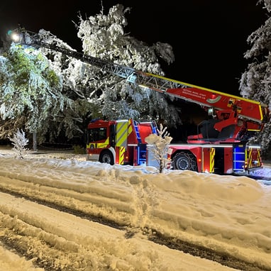 Feuerwehrfahrzeug mit Leiter im verschneiten Nachtwald.",