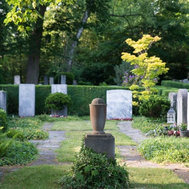 Grüner Friedhof mit Grabsteinen und Bäumen.