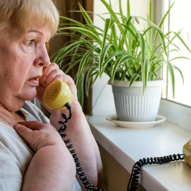 Ältere Frau telefoniert an einem Fenster.