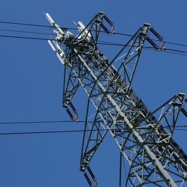 Strommast mit Hochspannungsleitungen gegen blauen Himmel.