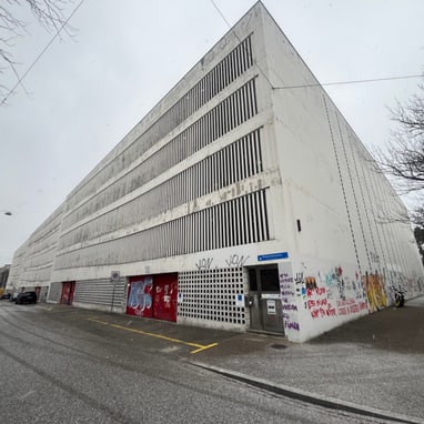 Grosses graues Parkhaus mit Graffiti an den Wänden an einem bewölkten Tag.