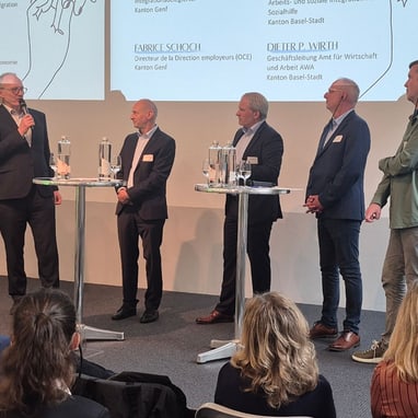 Männer auf Bühne bei Podiumsdiskussion mit Publikum.