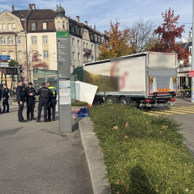 Strassenszene mit Polizeipräsenz neben einem Lastwagen und Wohnhäusern im Hintergrund.