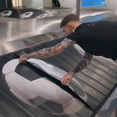Mann prüft Förderband mit Fussballmotiv am Flughafen.