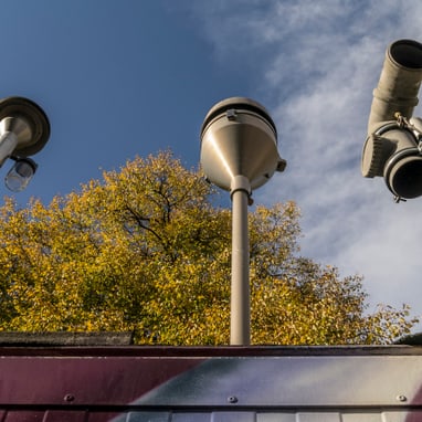 Strassenlaternen und Überwachungskameras vor Herbstbaum.