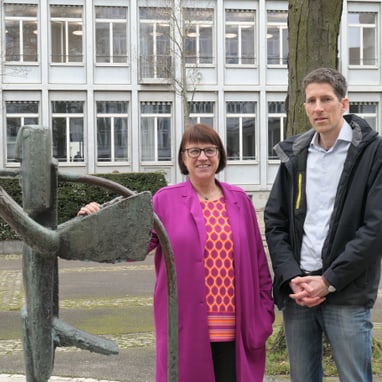 Zwei Personen stehen neben einer Skulptur vor einem Gebäude.