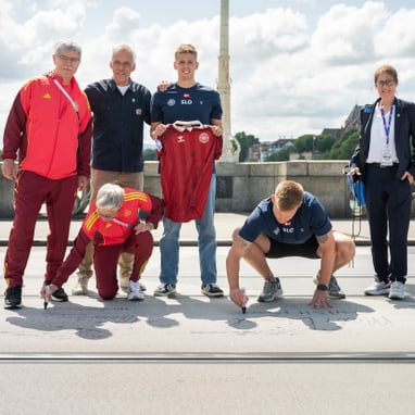 Gruppe von Personen auf einer Brücke, zwei knien und schreiben auf den Boden.