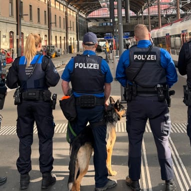 Polizisten und Hund auf Bahnsteig in Bahnhof.",